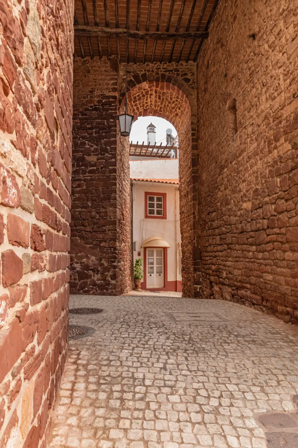 Calçada portuguesa e arcos históricos numa vila do Algarve sob céu cinzento