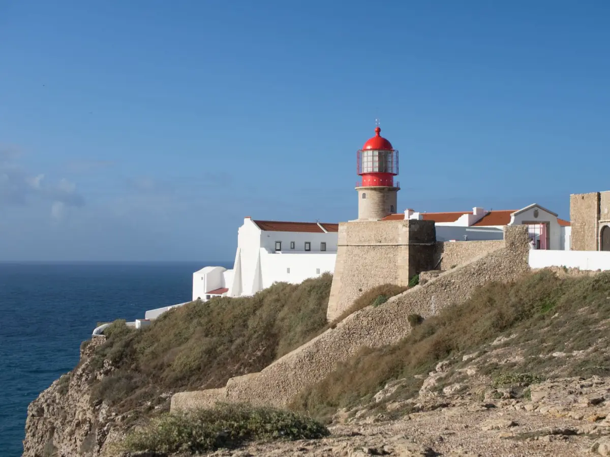 Farol branco no topo das falésias douradas de Lagos, com o oceano Atlântico ao fundo num dia limpo