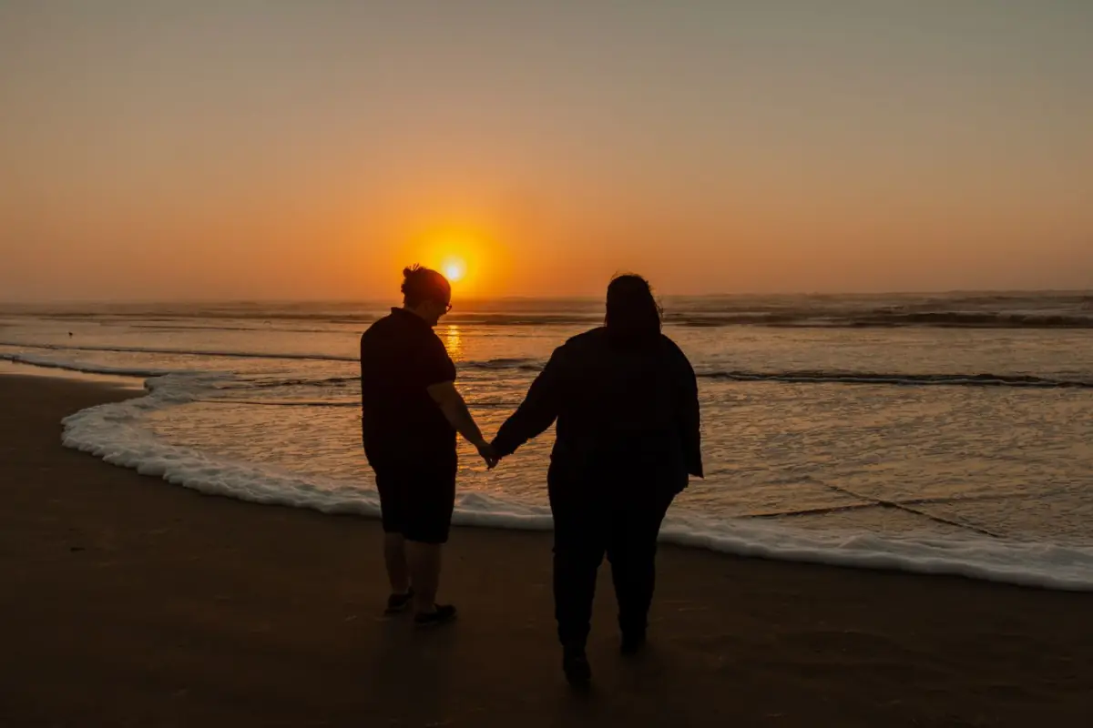 Casal de mãos dadas a caminhar à beira-mar numa praia algarvia ao pôr do sol