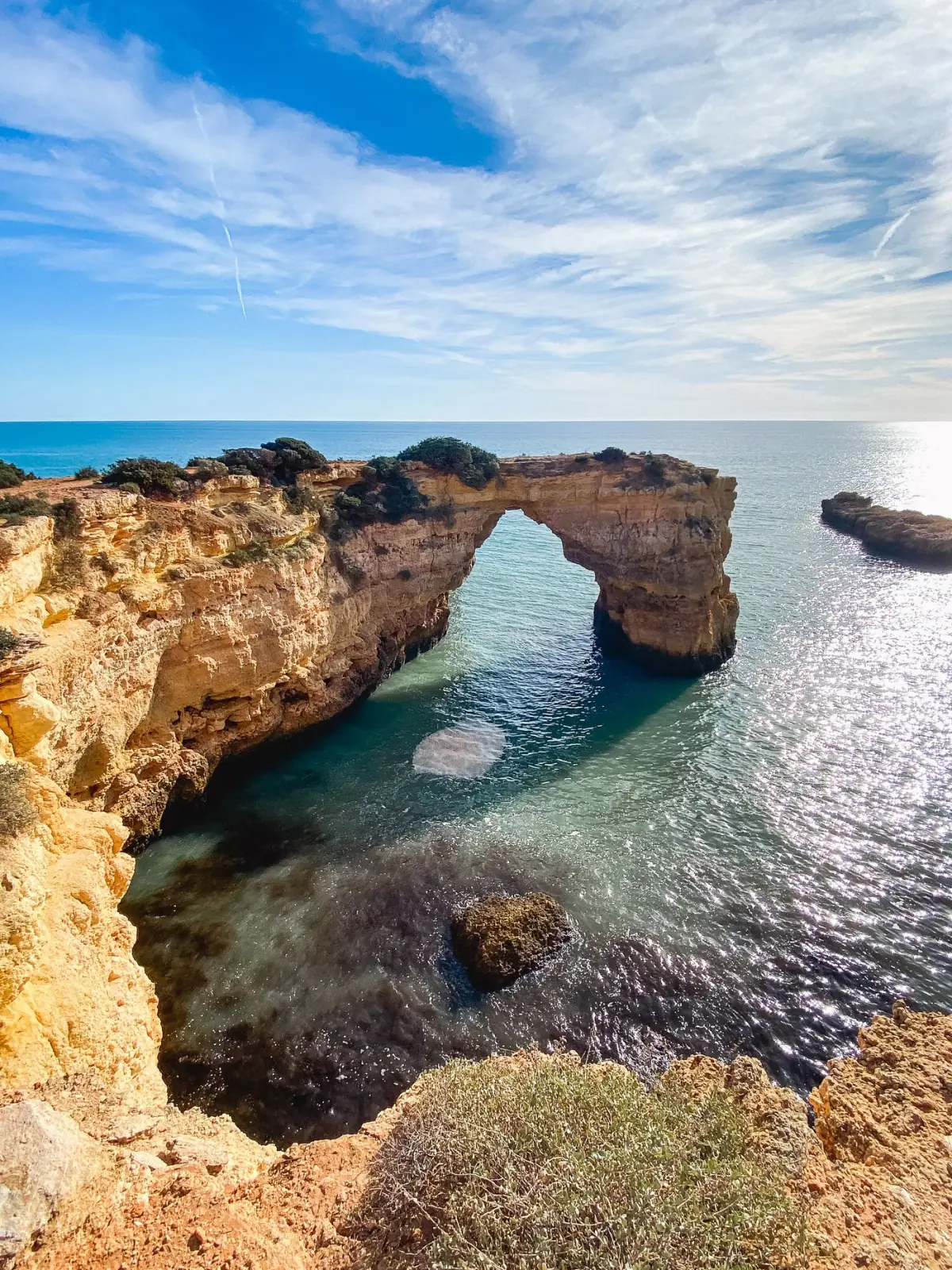 Formação rochosa em arco recortada pelo mar numa praia do Algarve ao entardecer