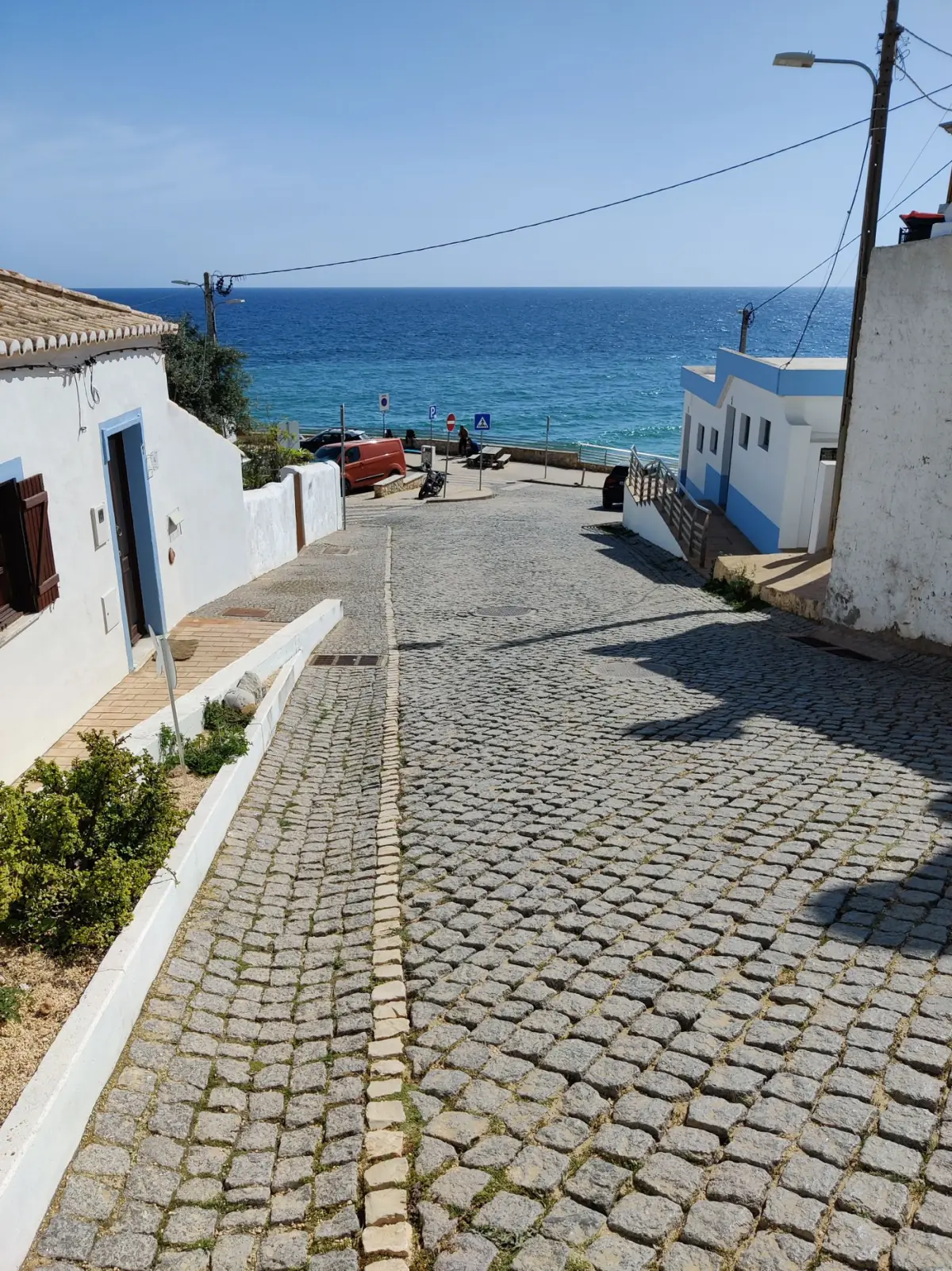 Rua de calçada portuguesa a descer até ao mar azul na Praia da Luz