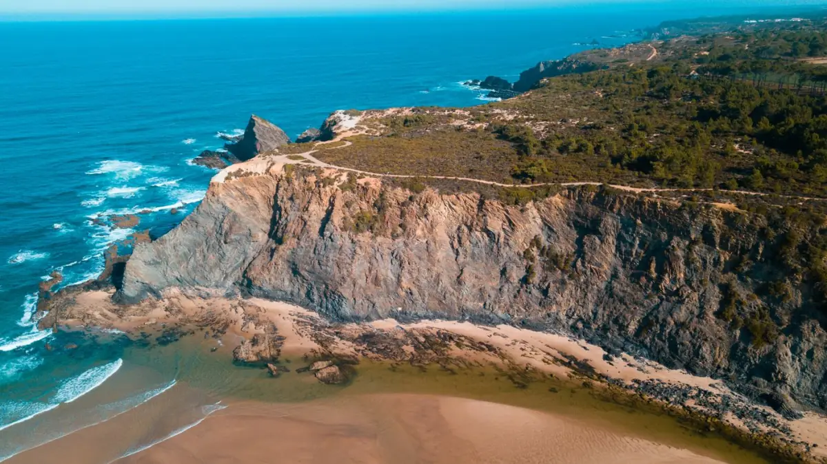 Falésias de xisto escuro e ondas a rebentar na praia de Odeceixe-Mar ao fim da tarde