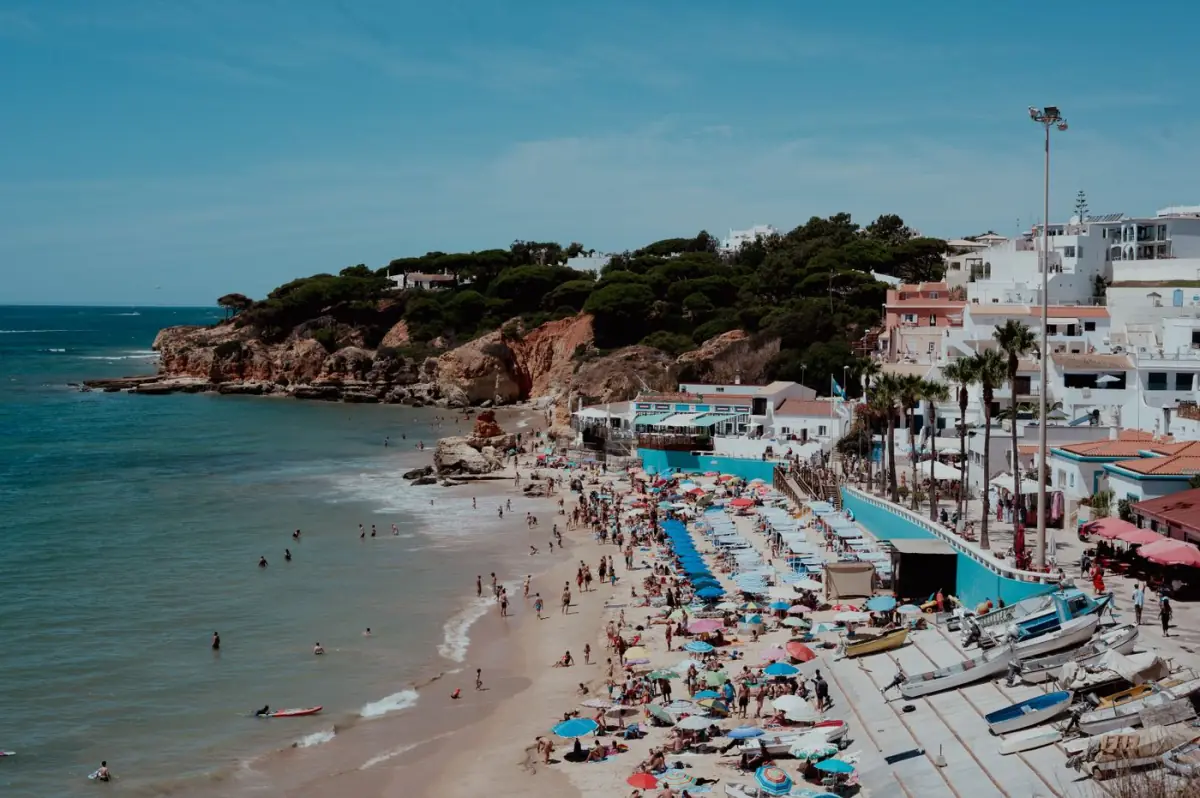 Praia do Barlavento algarvio com banhistas, guarda-sóis e falésias douradas ao fundo