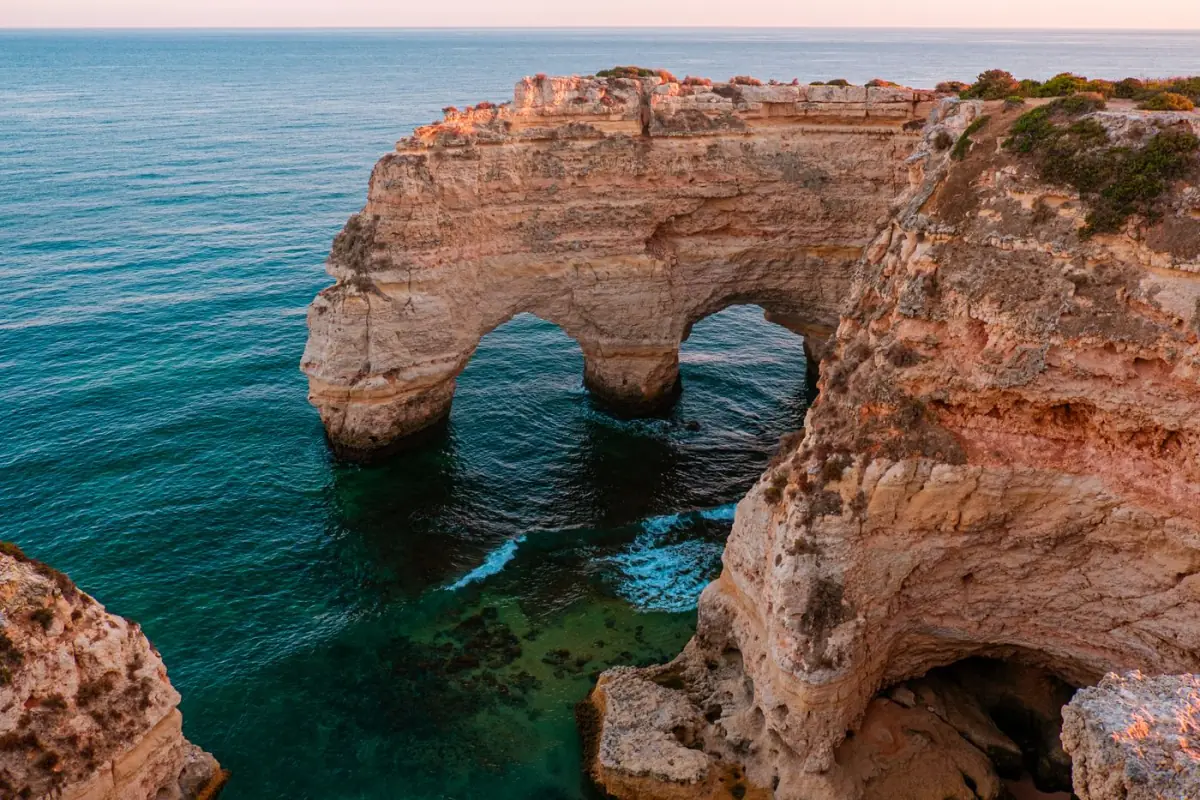 Falésias douradas do Algarve recortadas contra o Atlântico ao pôr do sol