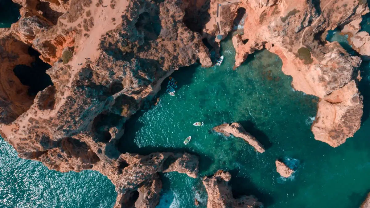 Vista aérea das falésias recortadas de Lagos, com enseadas de água azul e areais escondidos entre a rocha dourada