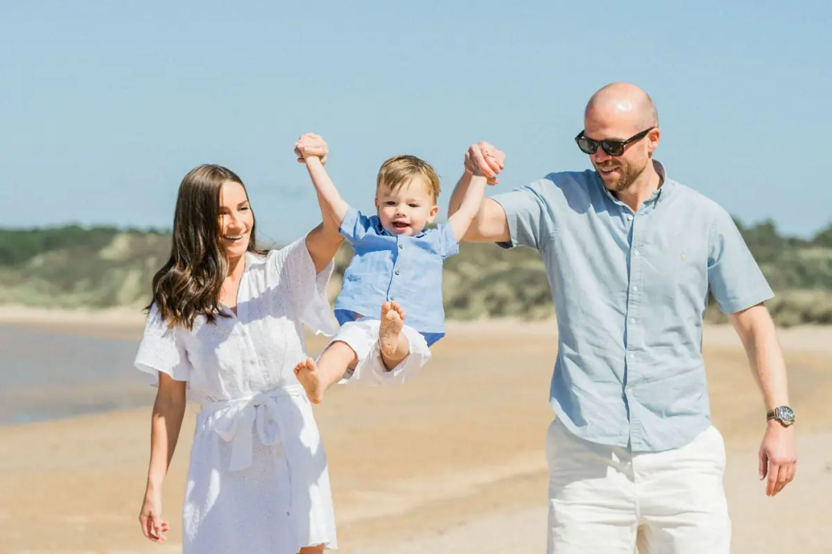 Pais a brincar com uma criança pequena na praia do Algarve ao final do dia