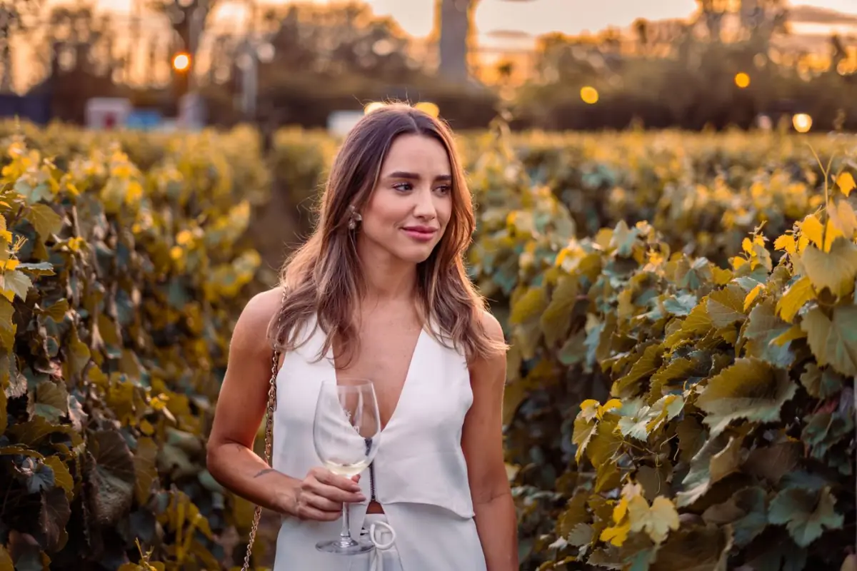 Visitante a passear entre as videiras de uma vinha algarvia ao pôr do sol com um copo de vinho na mão