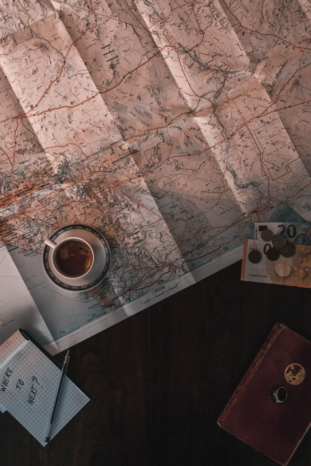 Mapa, café, moedas e bloco de notas sobre uma mesa — planeamento do orçamento de umas férias no Algarve