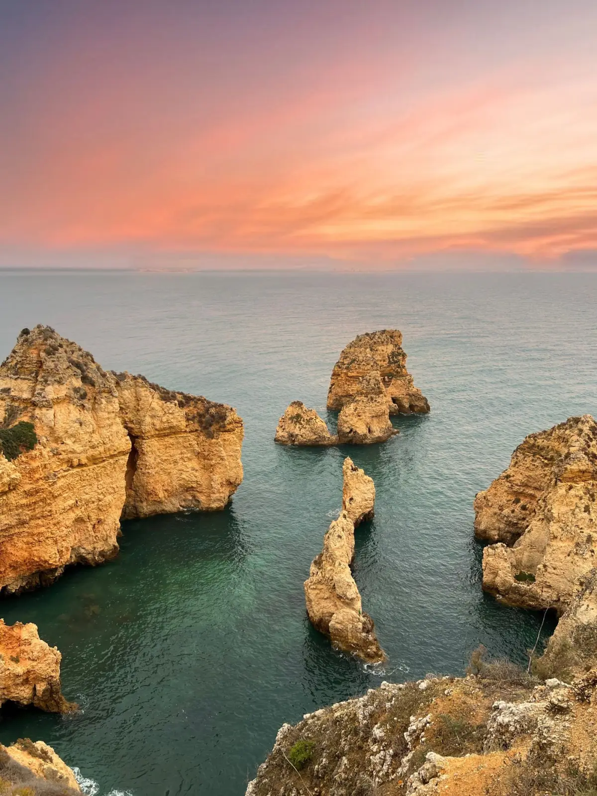 Pôr do sol alaranjado sobre as falésias e formações rochosas da Ponta da Piedade em Lagos
