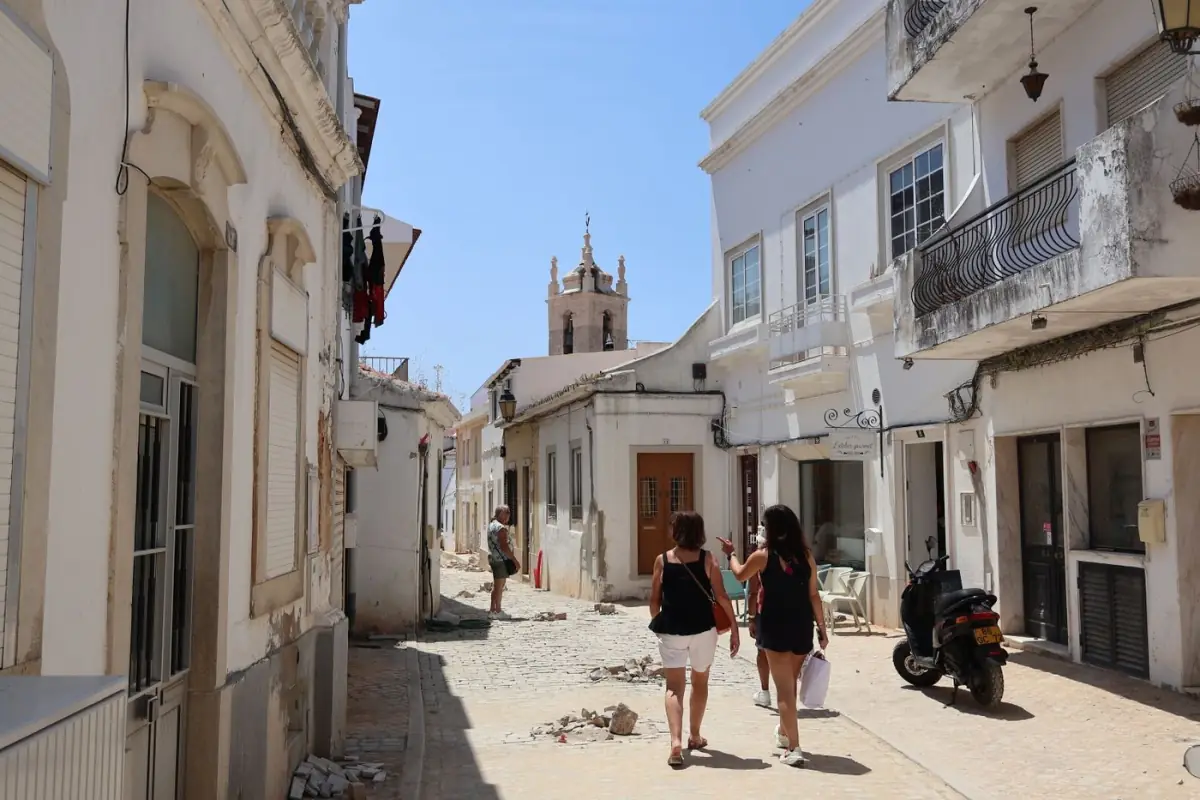 Rua de calçada portuguesa soalheira no centro histórico de Tavira, com fachadas caiadas e janelas tradicionais
