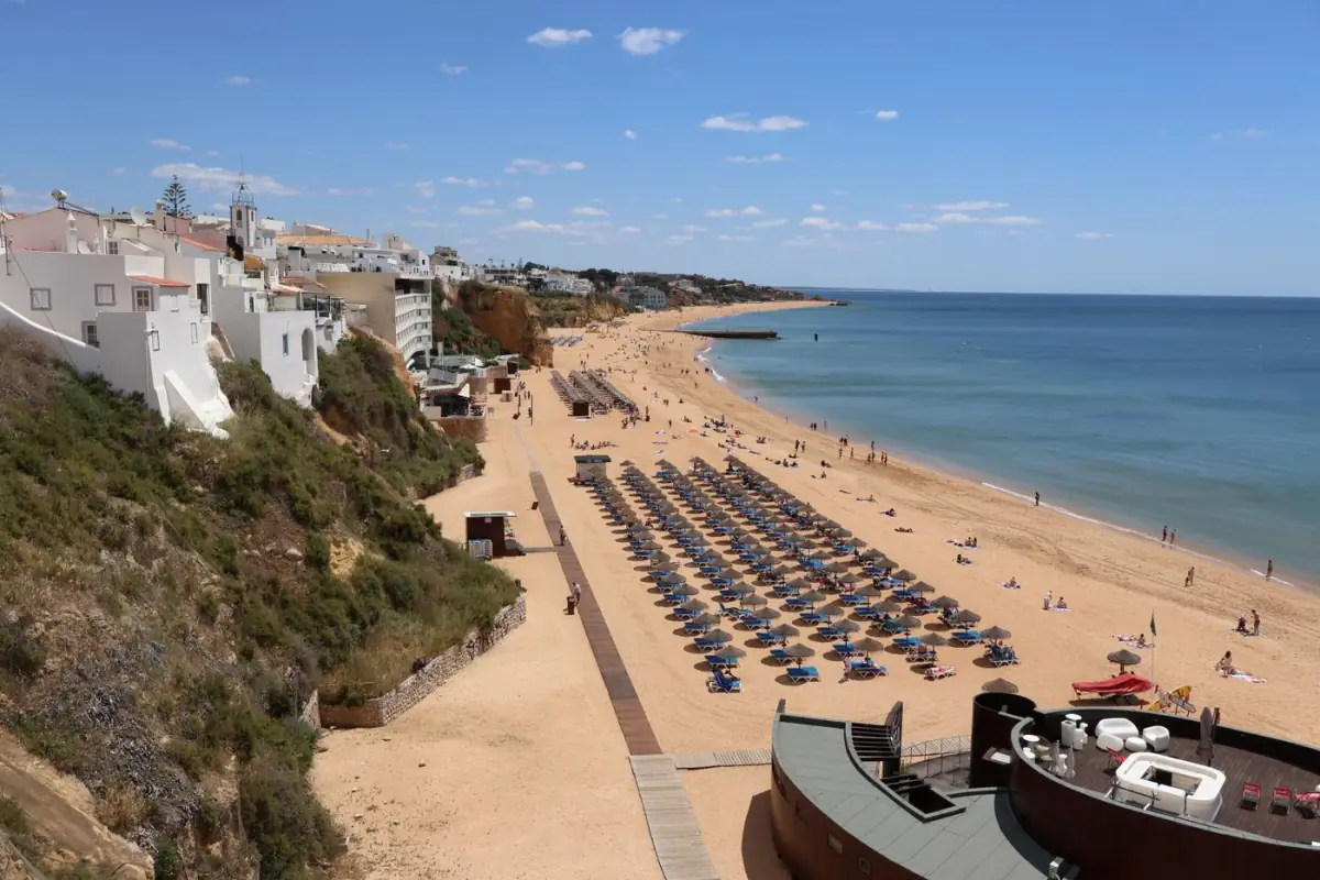 Praia de areia com falésias e guarda-sóis abertos num dia de sol no Algarve
