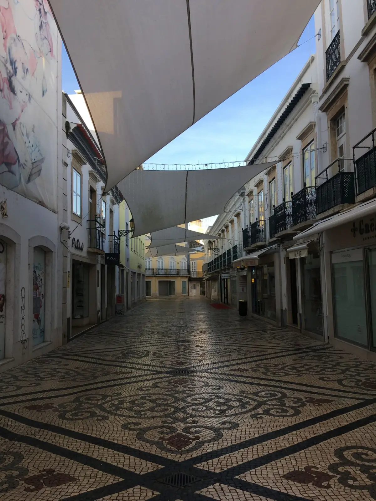 Rua de calçada portuguesa com toldos coloridos no centro histórico de Faro