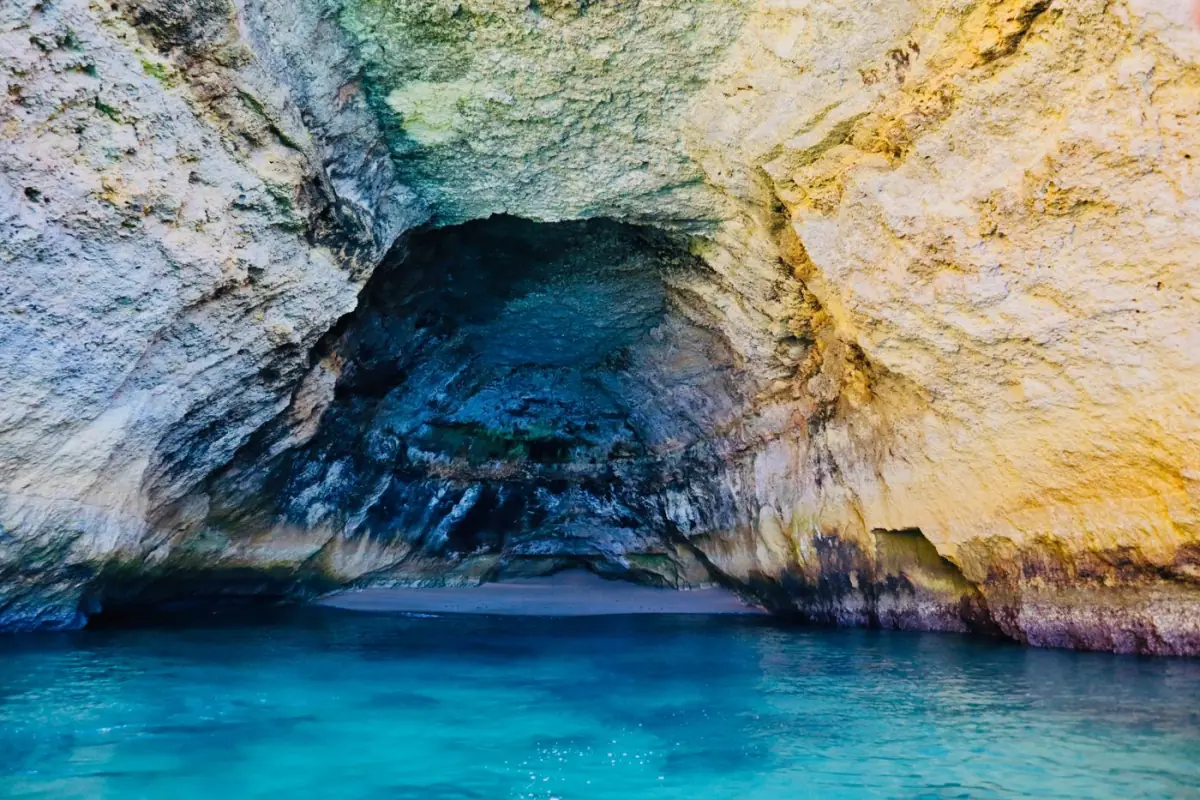 Caiaque a entrar numa gruta marinha do Algarve com águas azuis cintilantes e luz a entrar do tecto