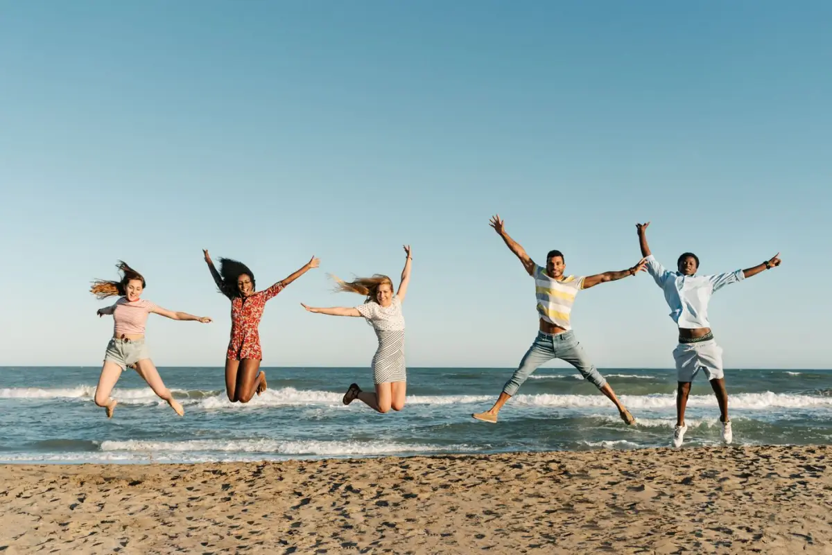 Grupo de amigos a saltar com os braços no ar numa praia do Algarve ao fim da tarde