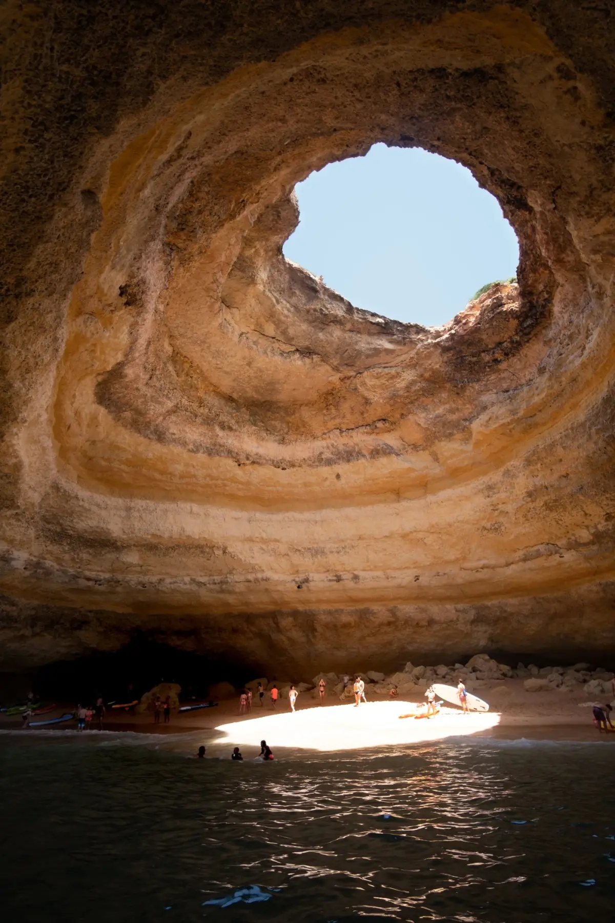 Interior da gruta de Benagil com a abertura circular no tecto a deixar entrar a luz do sol sobre a areia