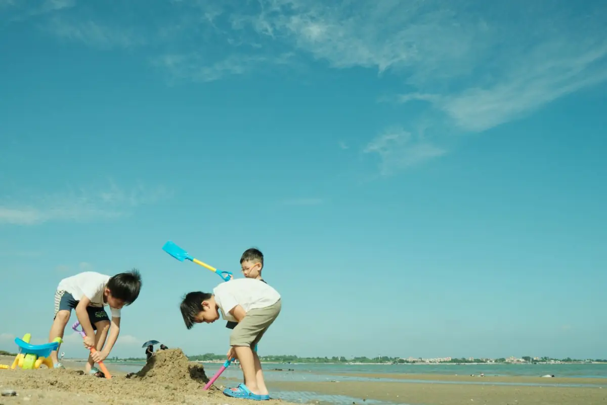 Crianças a cavar na areia com pás sob céu azul numa praia do Centro do Algarve