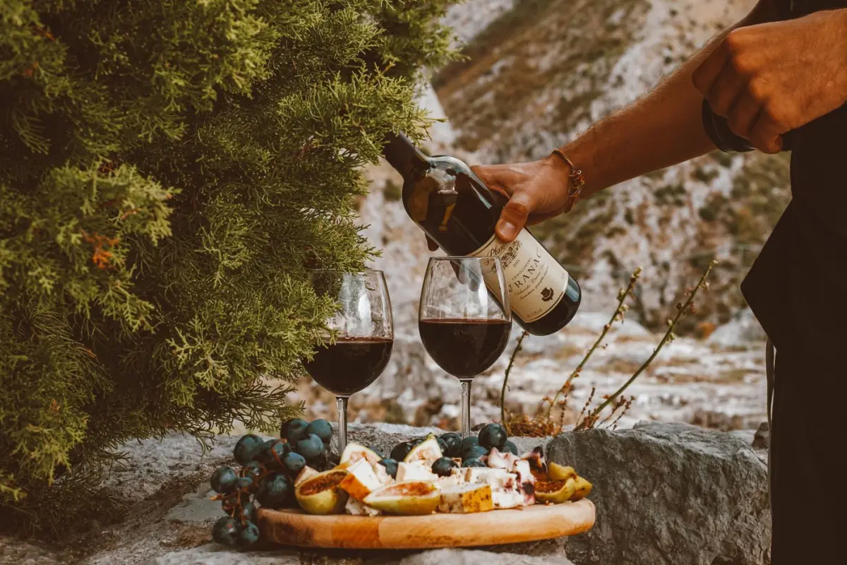 Tábua de prova com vinho tinto, queijo curado e cacho de uvas dispostos sobre uma pedra numa adega do Algarve