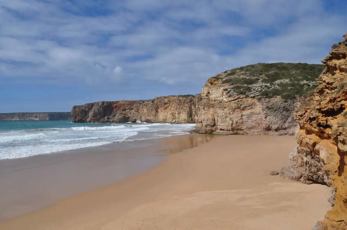Praia de Sagres com falésias douradas sob céu azul limpo