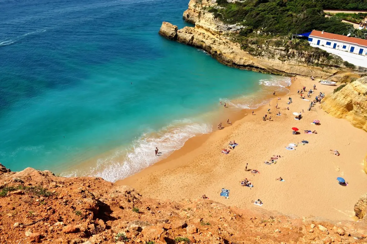 Praia cheia de banhistas e chapéus num dia de sol de verão no Algarve, em plena época alta