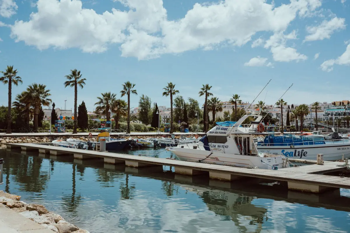 Marina tranquila no Sotavento algarvio, distrito de Faro, com barcos de recreio e palmeiras ao fim da tarde