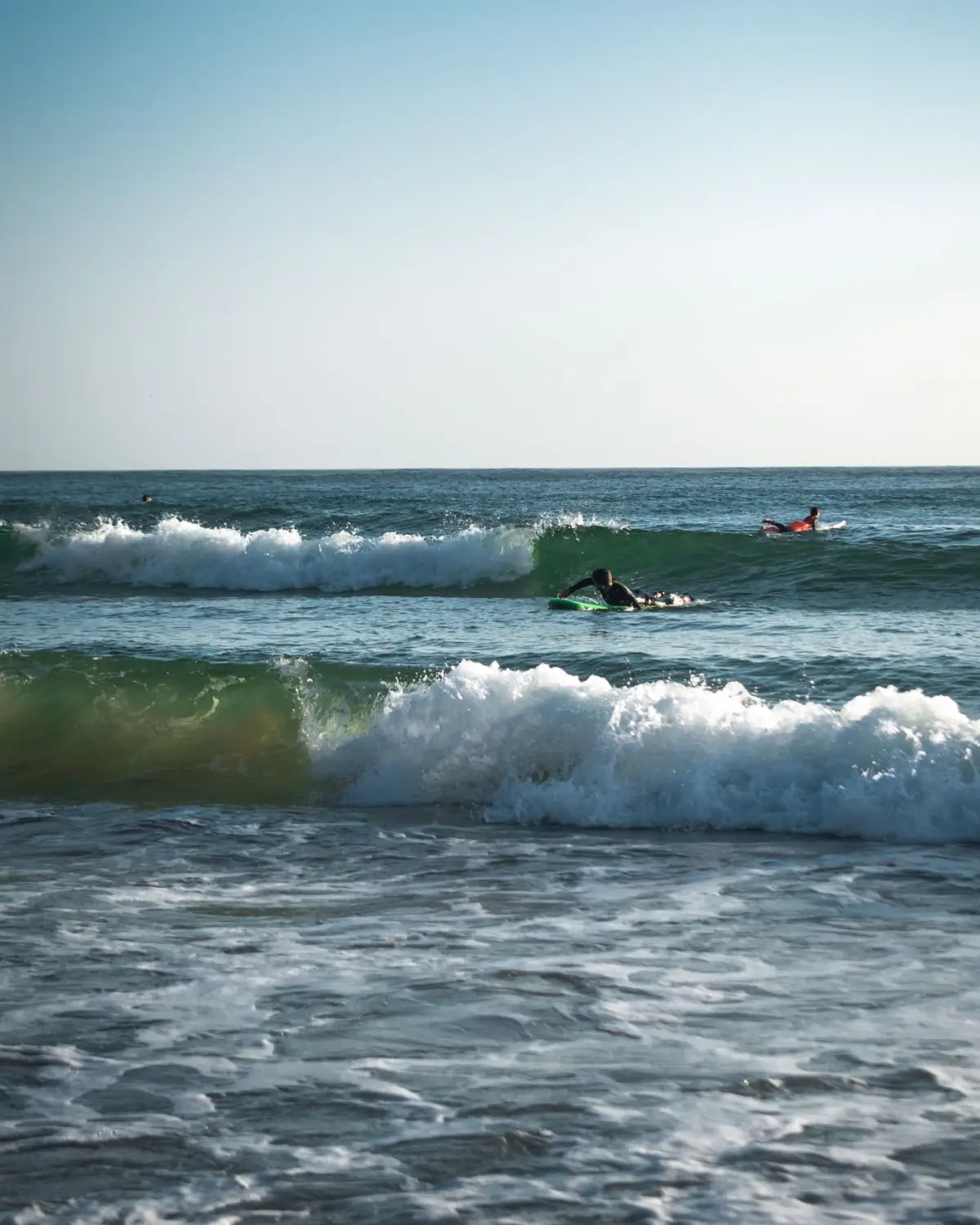 Surfistas a apanhar ondas numa praia da Costa Vicentina em Aljezur, com arribas ao fundo