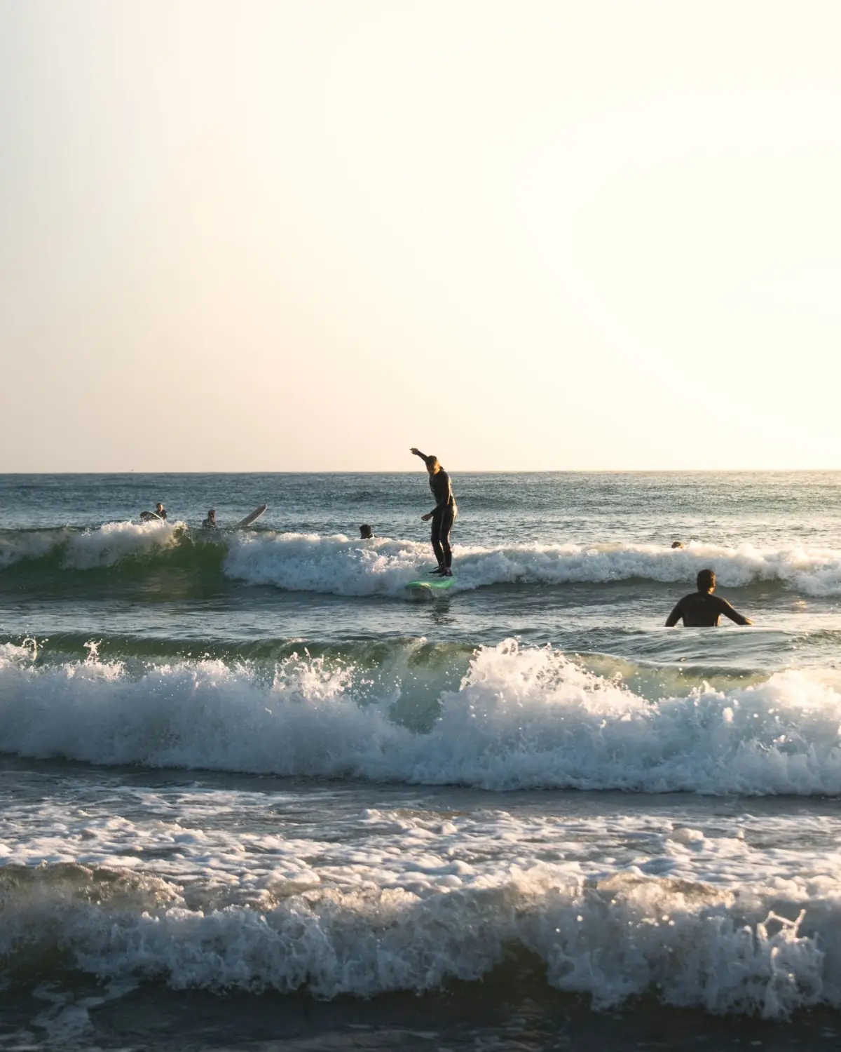 Surfistas na costa de Aljezur ao pôr do sol, com ondas a quebrar sob falésia