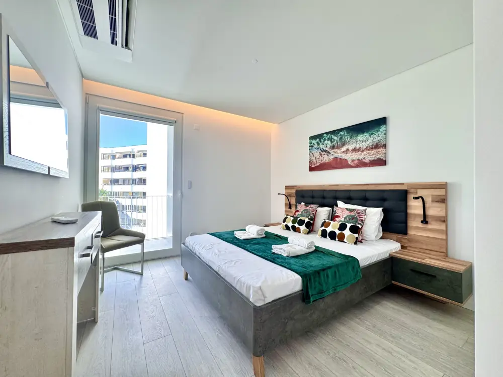 Bright bedroom with a made-up double bed, desk and open balcony door in a Vilamoura apartment